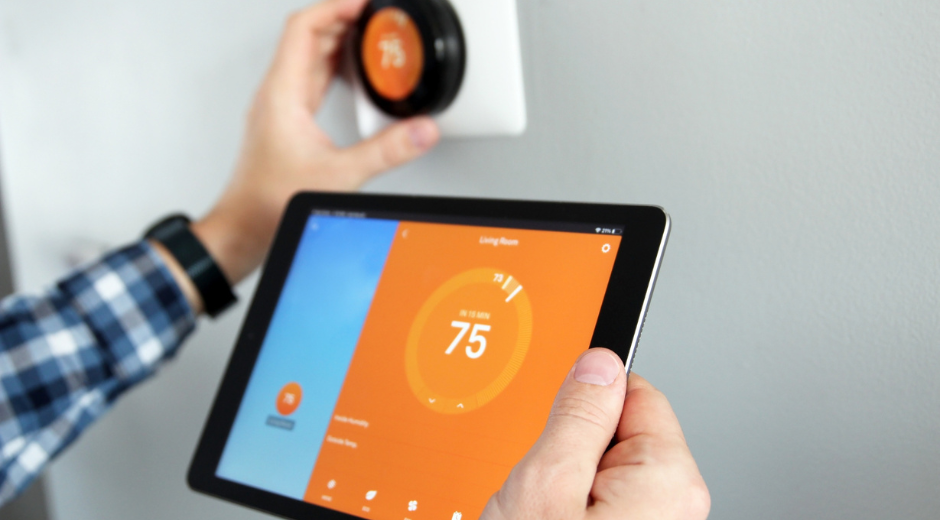 person holding a tablet with a smart thermostat in background